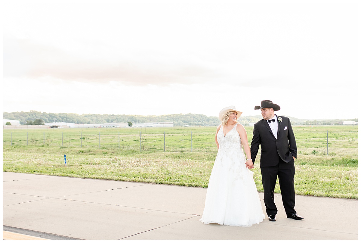 bride and groom wearing cowboy hats on airplane runway