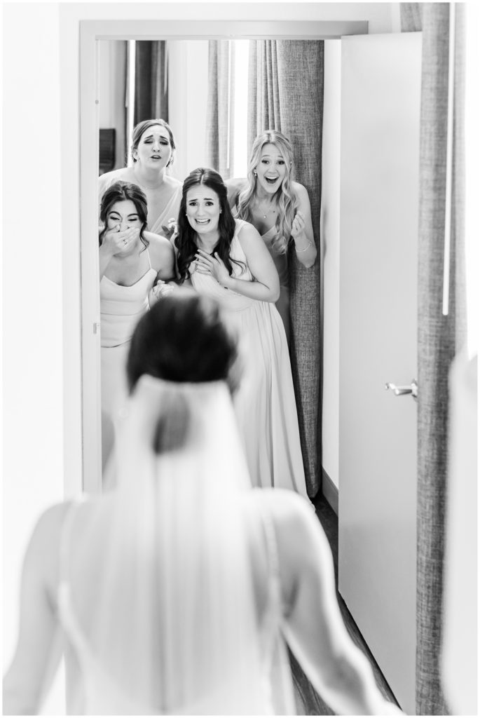 The bridesmaids react to the bride in her wedding gown.
