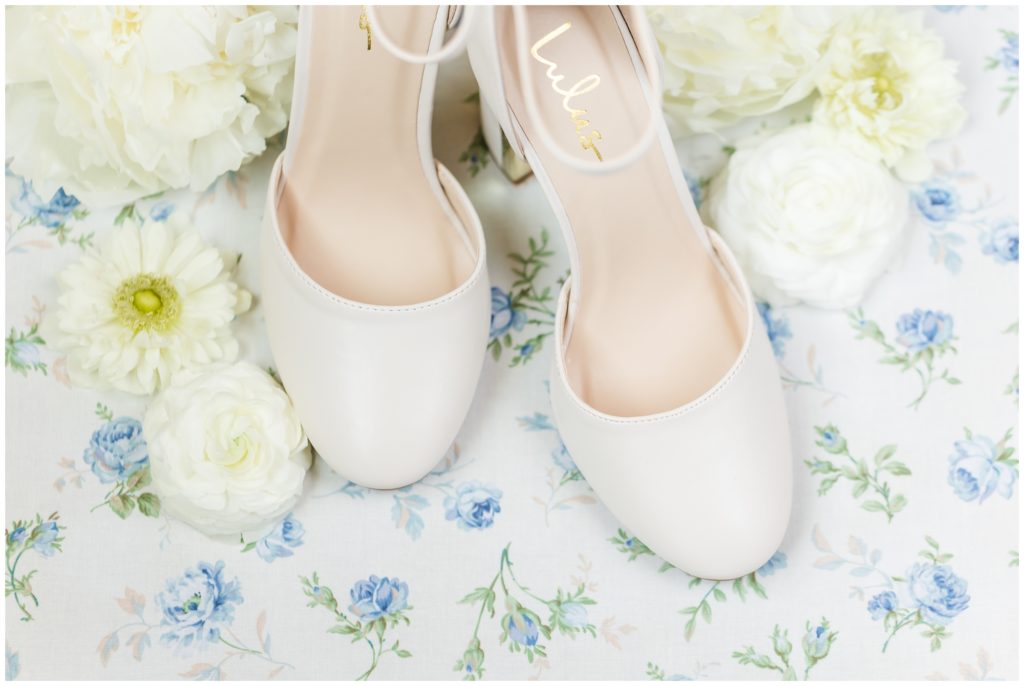 White round-toe wedding pumps on top of a light blue floral fabric piece are depicted. 