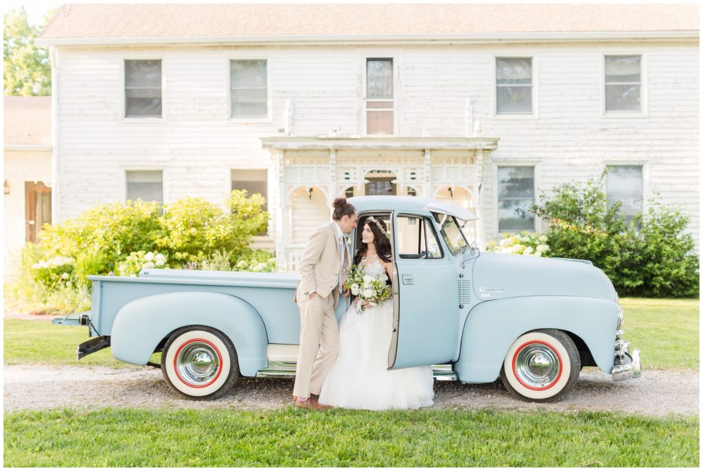 The bride and groom pose in a wedding portrait in front of a pale blue antique truck. 