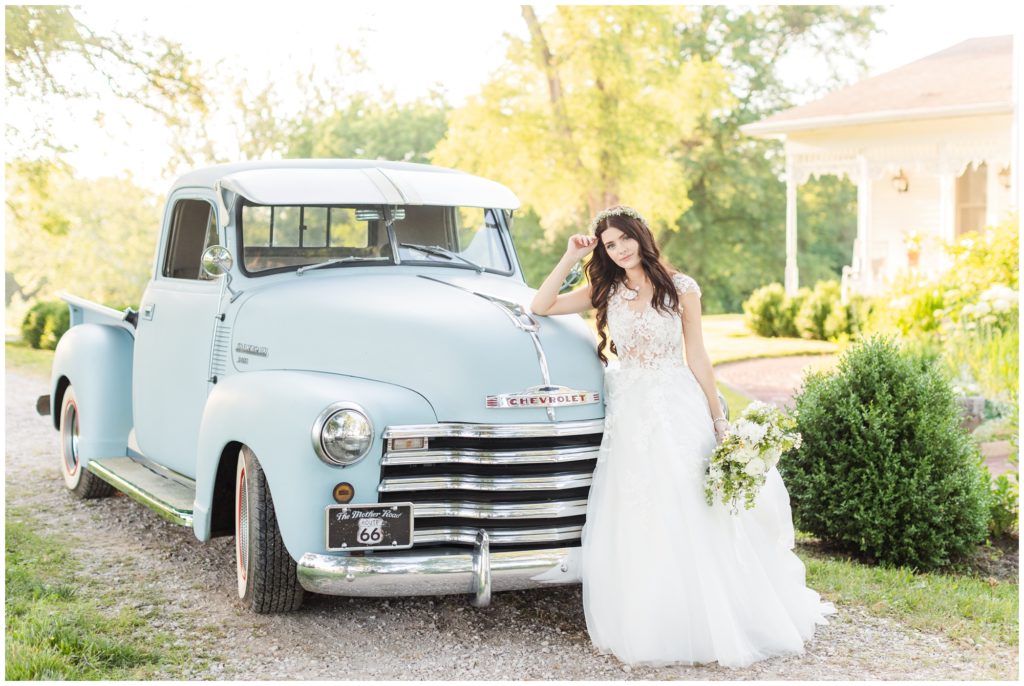 The bride poses in a wedding portrait in front of a pale blue antique truck. 