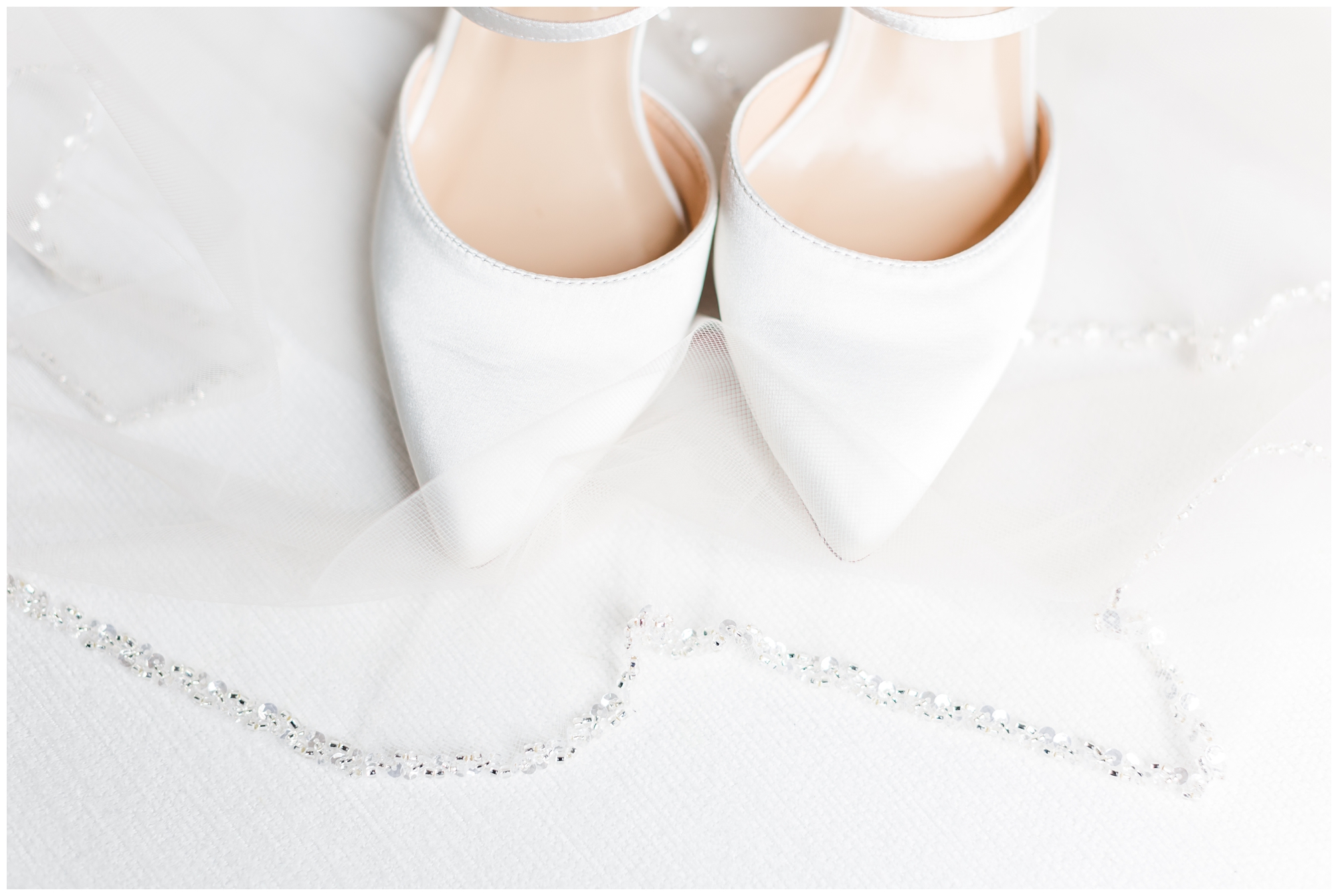 A pair of white pointy-toed bridal shoes are displayed on top of the bridal veil. 