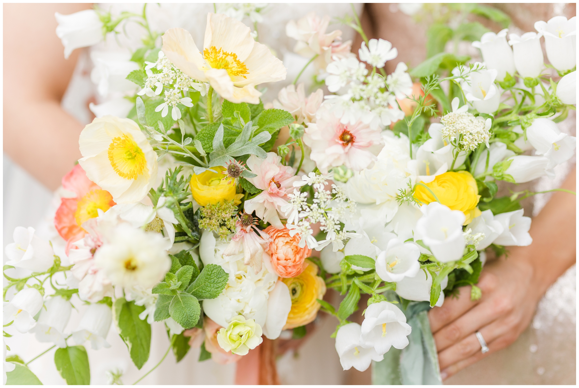 The wedding bouquet is held by the bride. It has pink, orange, yellow, and white flowers, also with greenery. 