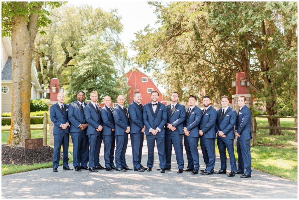 The groom and his groomsmen, dressed in dark blue tuxes, pose for a group picture. 