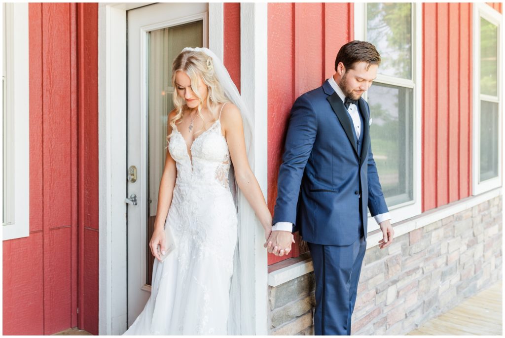 The bride and groom pose by a red building, holding hands around the corner. 