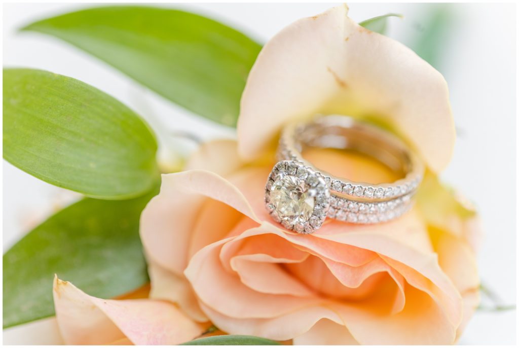 The bride's ring set is displayed on a peach rose. 