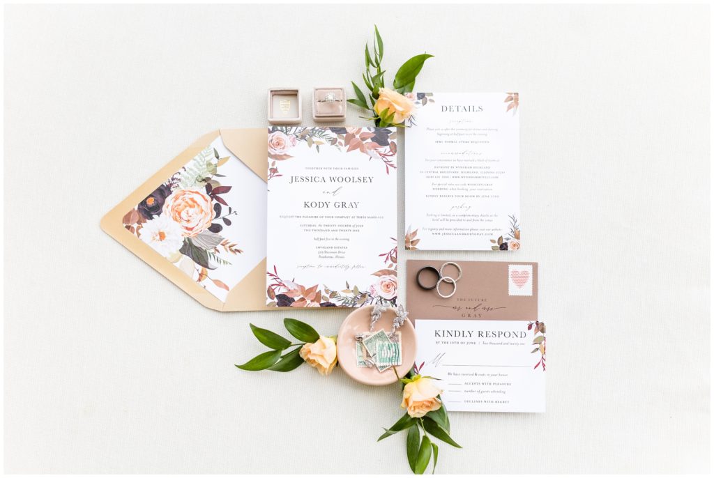 The floral invitation suite is displayed on peach roses. 