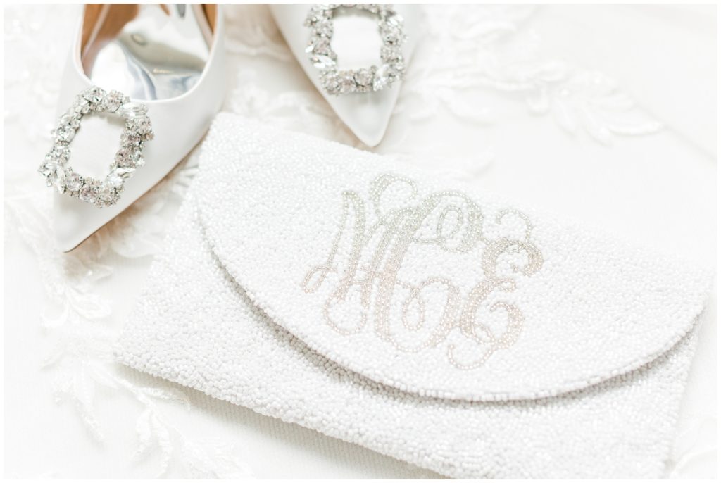 The bride's white Badgley Mischka wedding shoes are displayed with a white beaded and monogrammed clutch. 