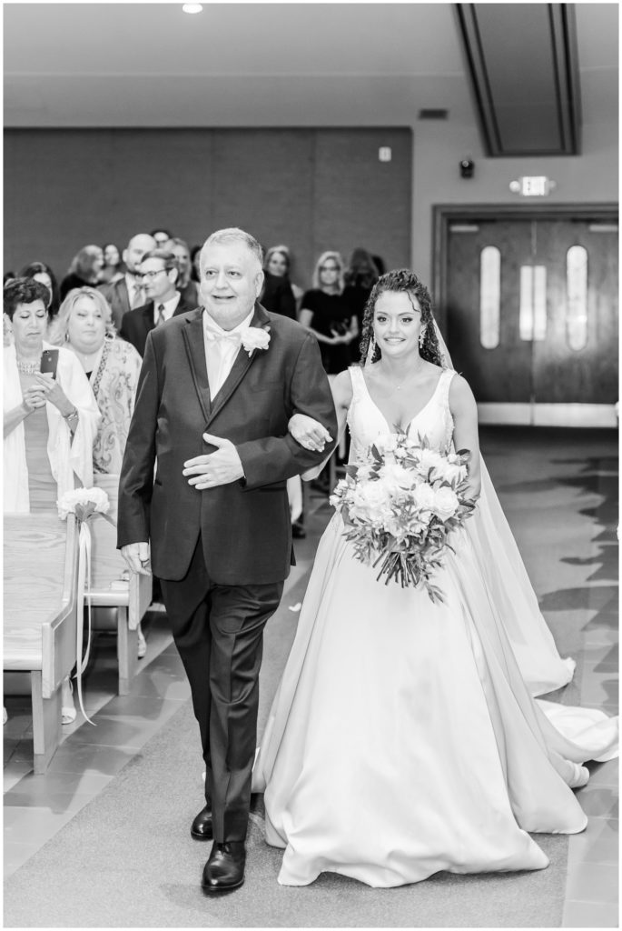 The bride walks down the aisle escorted by her father. 
