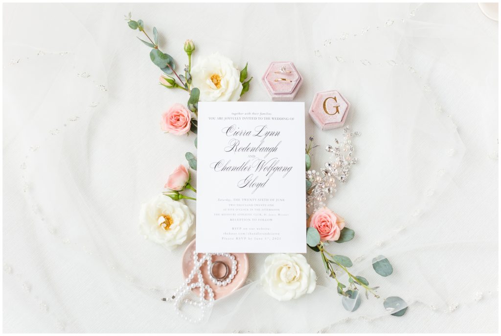 Wedding invitation suite displayed on a background of light pink and white florals. 
