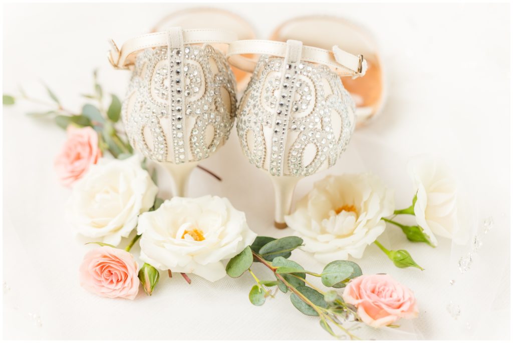 The bride's creamy white wedding shoes, adorned with a lace-inspired crystal design, are show on her wedding flowers - white and pale pink. 