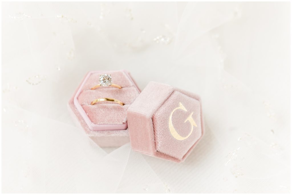 Picture shows the engagement ring and bride's wedding band in a light pink ring box monogrammed with a gold "G"