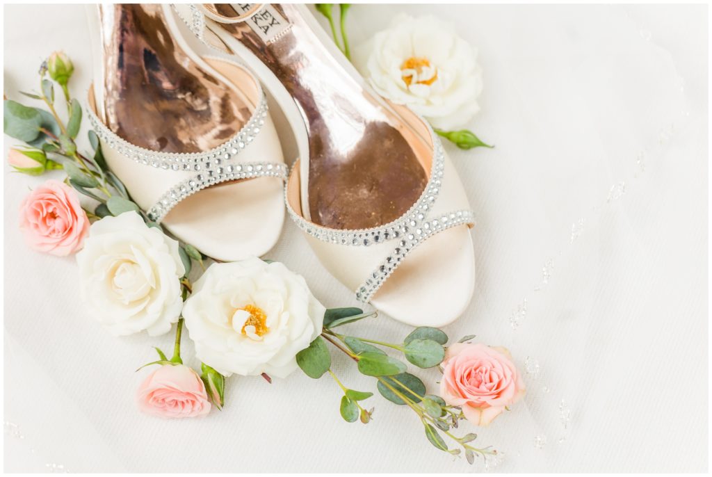 The bride's creamy white wedding shoes, adorned with a lace-inspired crystal design, are show on her wedding flowers - white and pale pink. 