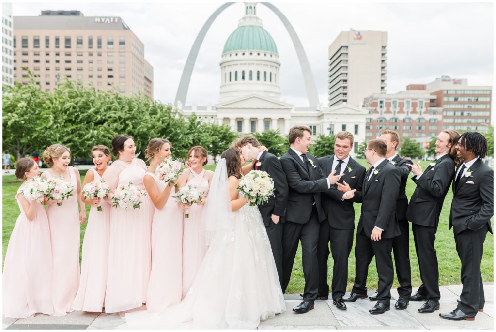 The wedding party poses for a group photo with the st louis arch in the background. 