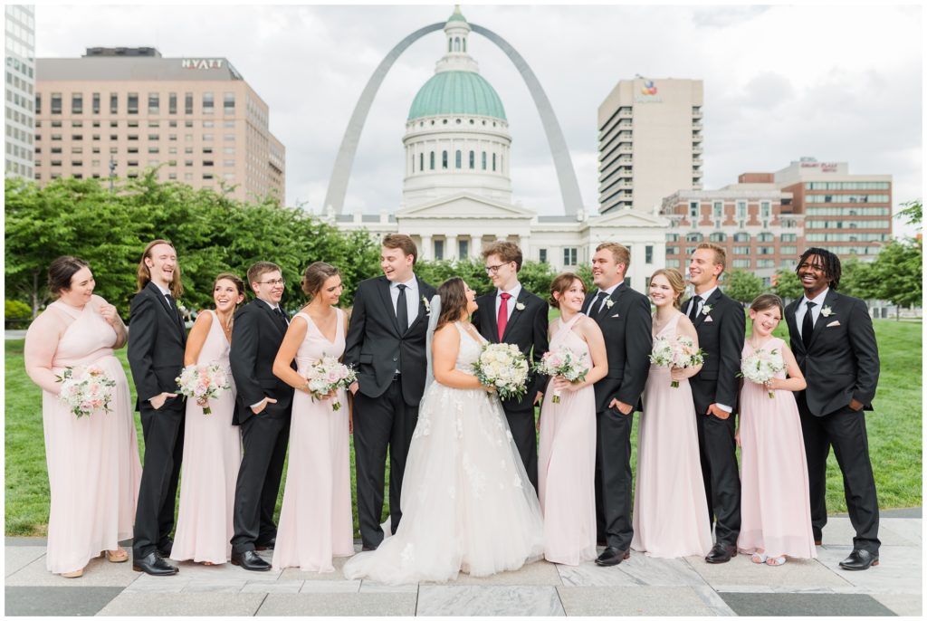 The wedding party poses for a group photo with the st louis arch in the background. 