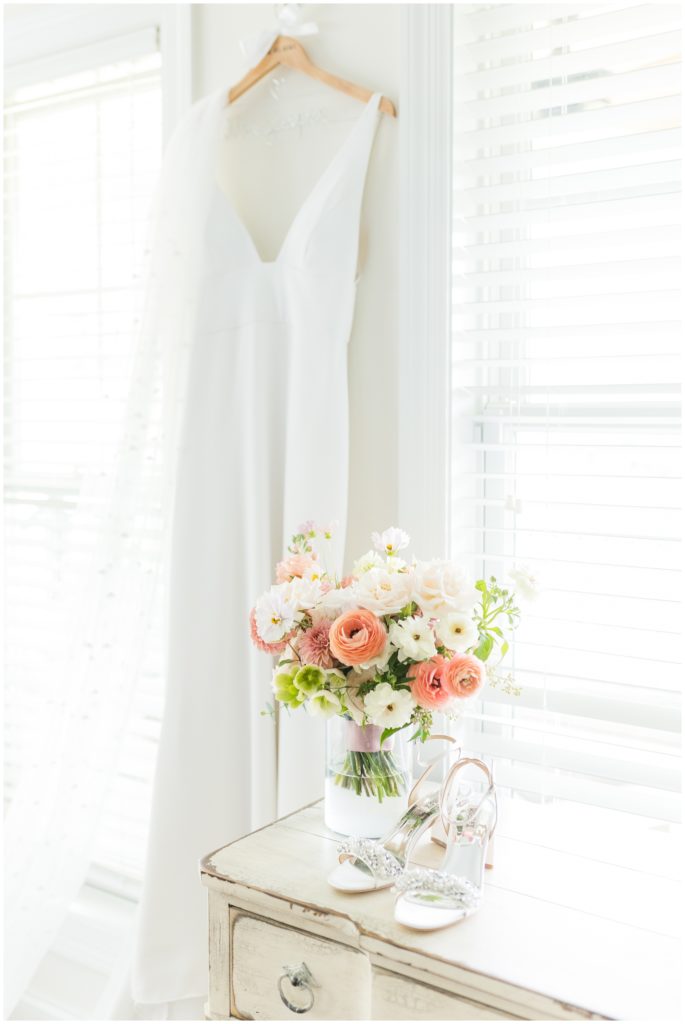 The english garden style bouquet is pictured with pale peaches and pinks, along with bright white and soft green. Next to it are a pair of white Badgley Mischka wedding shoes. 