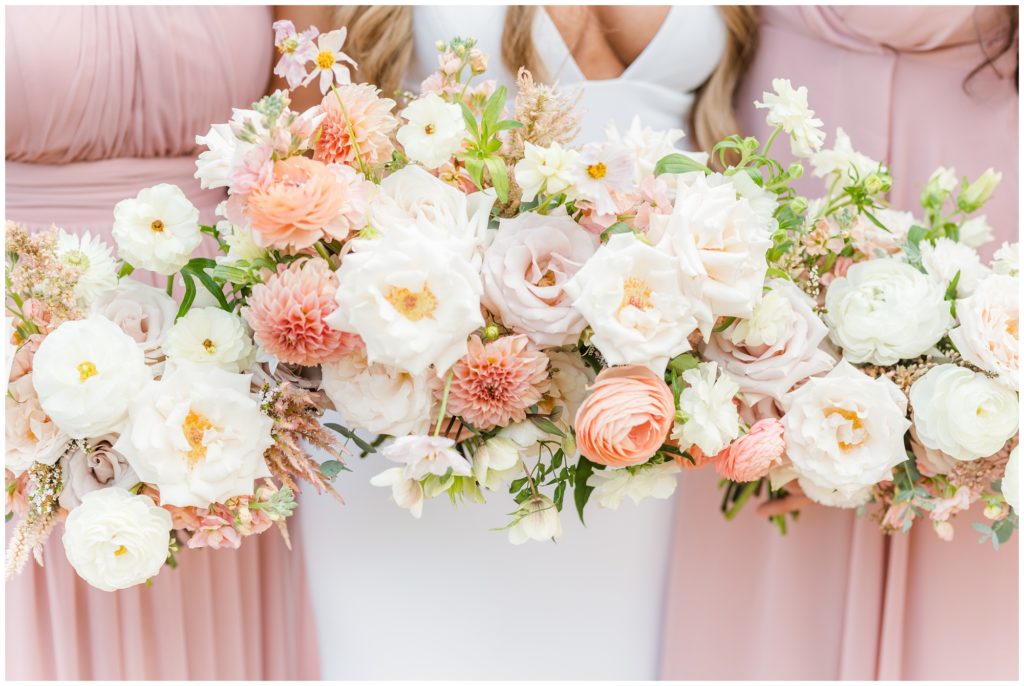 The bridal party holds their english garden style bouquet is pictured with pale peaches and pinks, along with bright white and soft green.
