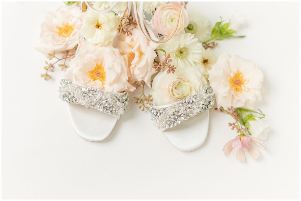 The bride's Badgley Mischka crystal studded wedding shoes are topped with pale peach and white garden florals. 