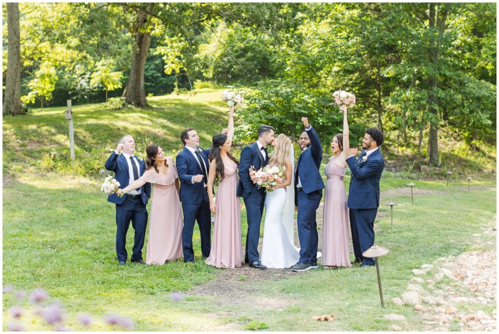 The bridal party is pictured. The bridesmaids are in a blush pink floor-length gown and the men are wearing blue suits. 