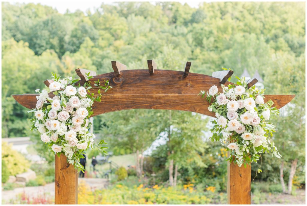 the wooden wedding arch, topped with blush pink florals, is displayed. 