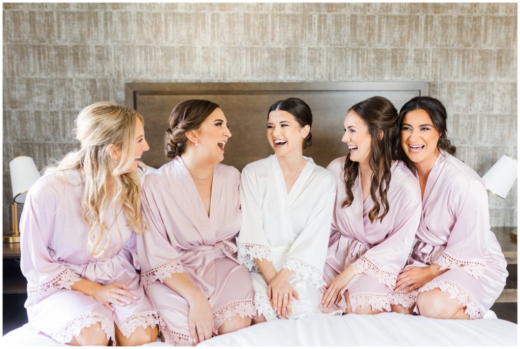 The bride laughs with her attendants in matching robes. 