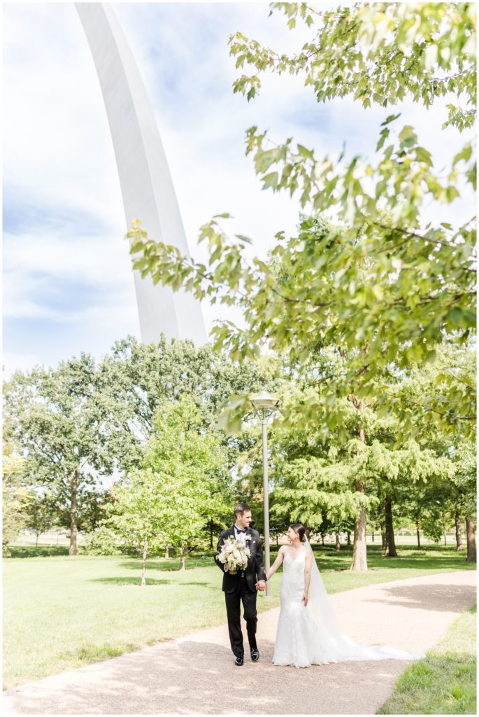 The bride and groom are pictured in a portrait underneath the st louis arch. 